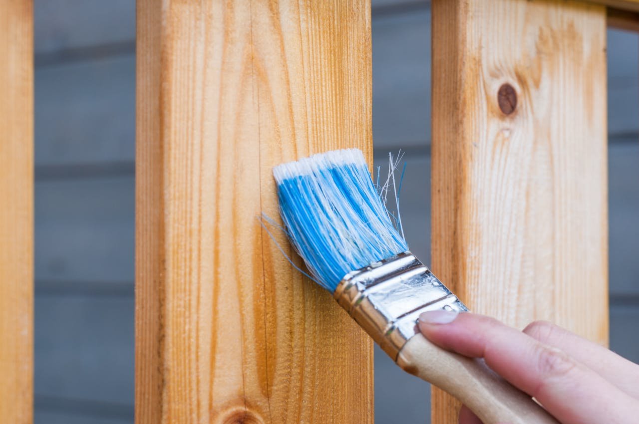 Crafting Captivating Headlines: Your awesome post title goes here A hand painting a wooden fence plank with a blue paintbrush outdoors. Perfect for DIY and renovation themes.